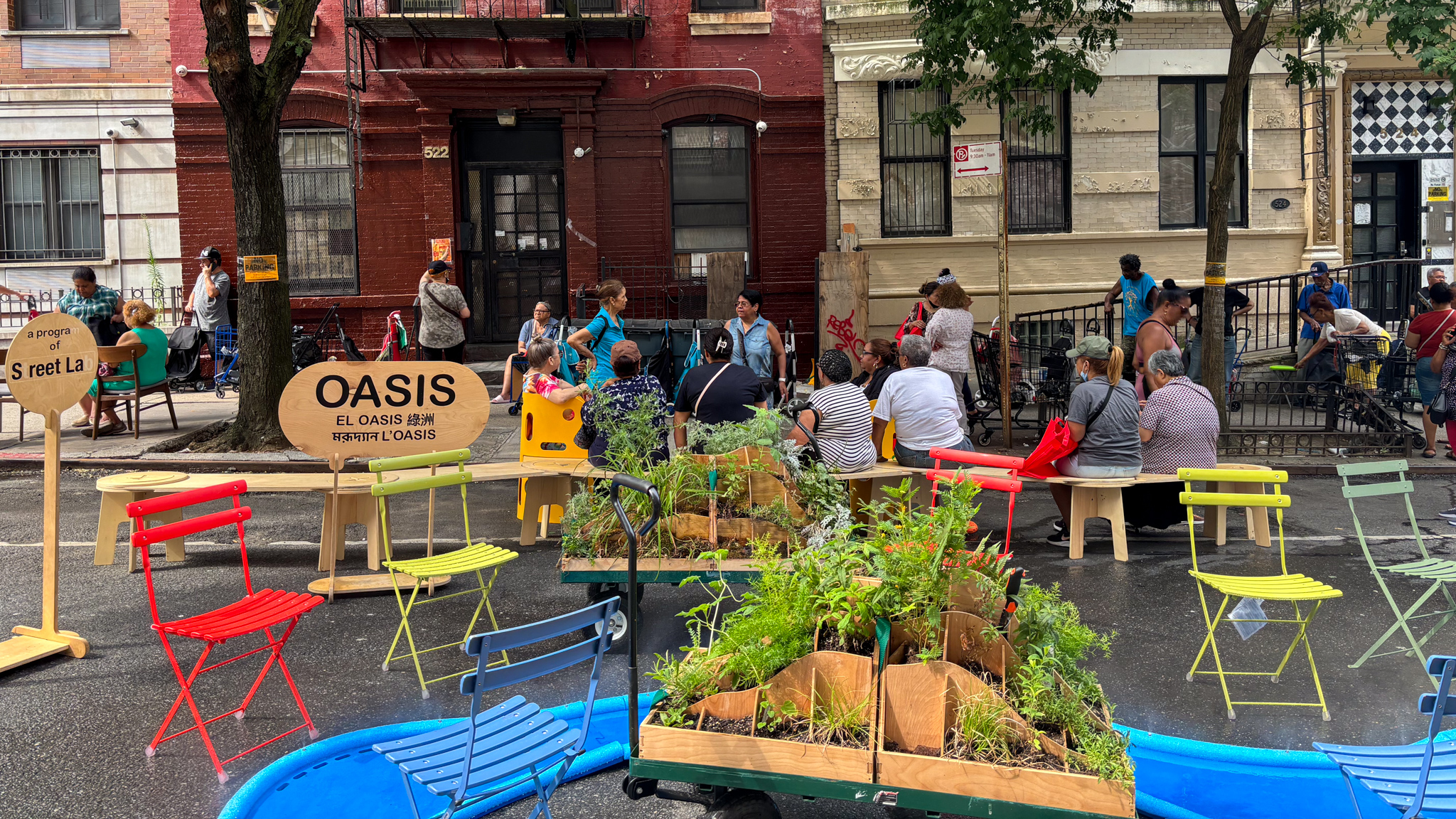 People sitting around a blue, river-like misting structure and planters on the street.